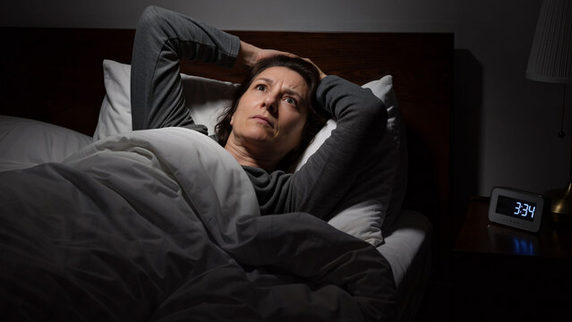 Woman unable to sleep, lying in bed with her hands behind her head, awake in the darkness. Insomnia and anxiety concept.