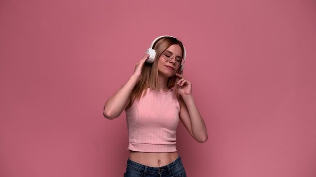 Young woman wearing headphones dancing and listening to her favorite music playlist on a pink studio background