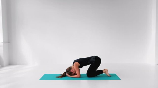 Flexible woman performing a yoga headstand exercise in a bright studio isolated on a white background