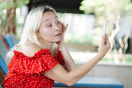 Caucasian woman checking her cosmetics make up with smartphone mirror mode