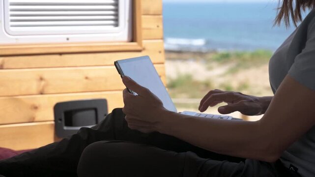 Digital nomad woman typing on a laptop computer inside a camper van with a sea view