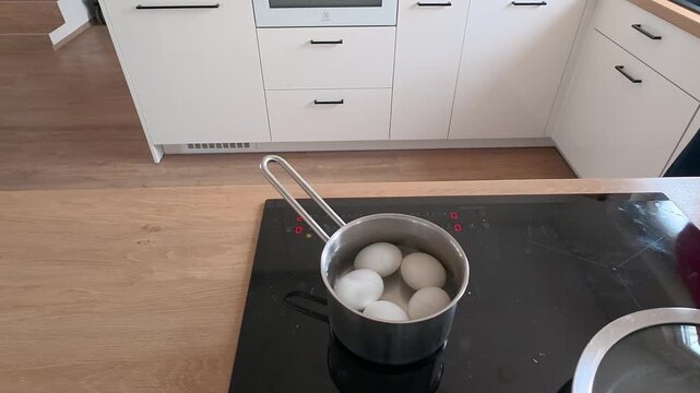 Close-up shot of boiling eggs on a sleek induction cooktop in a modern kitchen. The pot gently simmers, capturing the contemporary culinary process with crisp lighting and clear focus.