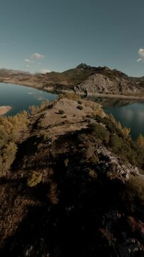 Dynamic vertical FPV cinematic flight over the rugged landscape of Porma Reservoir in Leon, Spain, featuring calm blue water and rocky peaks.
