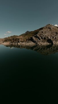 A cinematic vertical FPV drone shot flying over the calm waters of Porma Reservoir towards rugged mountain peaks in Leon, Spain. Ideal for travel social media and nature documentaries.