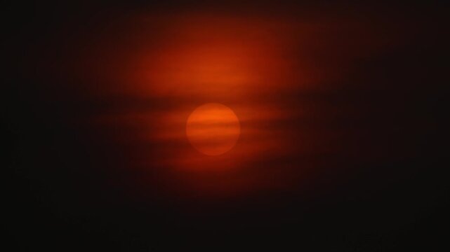 Dramatic sunset with a large orange sun glowing through thick clouds and mist. Cinematic atmosphere at dusk or dawn.