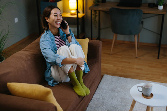 Young woman having relaxed phone conversation with coffee on sofa at home