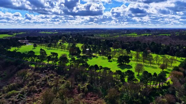 Aerial drone shot of a WWII American military cemetery with white grave markers among green woodland. Normandy, France