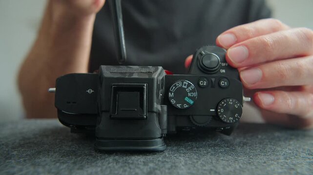 Person's hands using a dust blower tool to clean sensitive camera sensor and mirrorless body for maintenance.