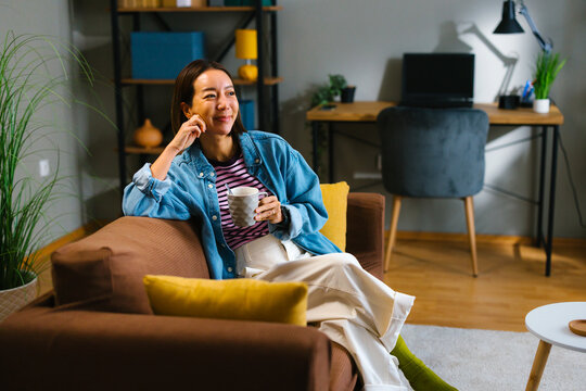 Young woman relaxing with coffee and smartphone on sofa at home