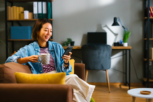 Young woman drinking coffee and using smartphone while relaxing at home