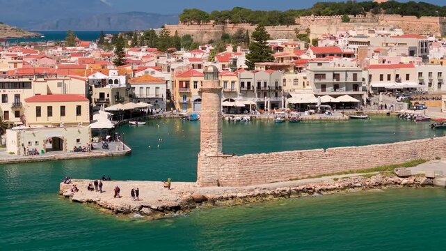 Rethymno Lighthouse Crete Greece aerial 70mm close up orbit of Venetian harbor, old town with pastel houses and Fortezza castle, cinematic drone shot of landmark and people walking by sea