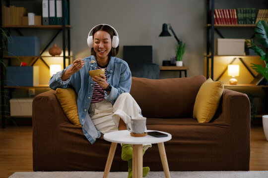 Happy asian woman relaxing at home eating cereal and listening music