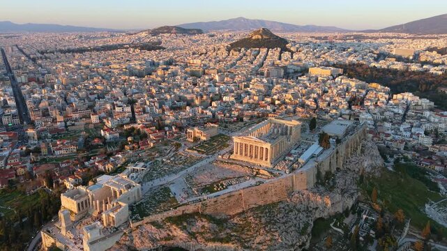 Aerial video of the ancient Parthenon temple atop the Acropolis hill, showcasing the dense urban landscape of Athens during the golden hour.