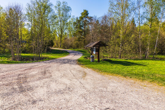 Beautiful view of gravel road at fishing base with information stand and waste barrel near trees. Sweden.