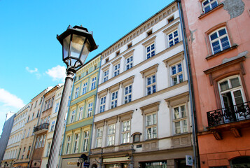 Obraz premium Colorful historic townhouse line a charming street in Krakow old town under a bright blue sky. Classic European street lamp in the foreground. Old street flats. 
