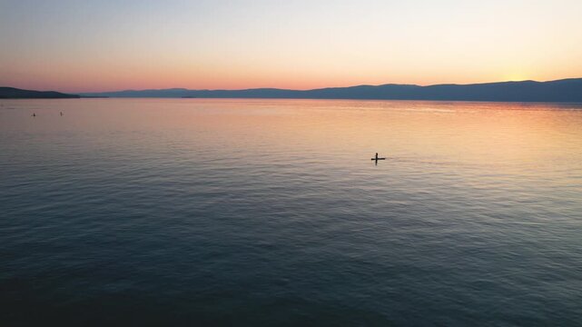 Lake Baikal, summer evening. Flight over Cape Burkhan or Shamanka Rock on Olkhon Island. Tourists paddleboard in the bay. Active recreation.