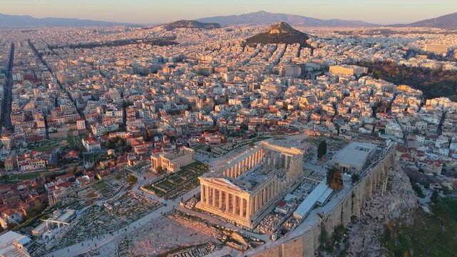 Aerial video of the ancient Parthenon temple atop the Acropolis hill, showcasing the dense urban landscape of Athens during the golden hour.