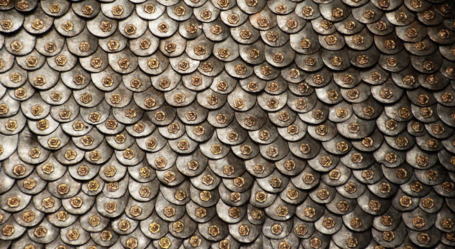 Close up of medieval armor with detailed metal scale pattern texture. Steel plates create a strong repeating background with historic feel. Metallic surface shows vintage armor design.