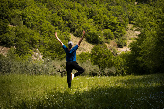 Mindful person practicing yoga tree pose admits lush green nature, connecting with the earth. 