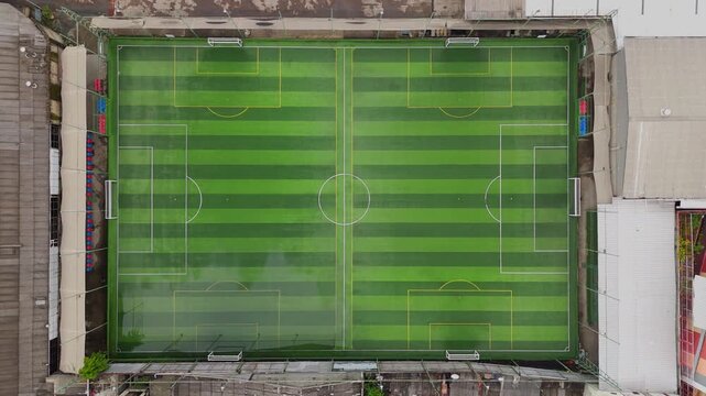 Static aerial top view of a green futsal field with striped turf and white markings in urban setting