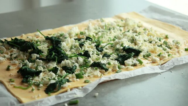 Close-up of adding cooked baby spinach over cheese and green onions on raw puff pastry