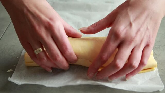 Close-up of woman's hands rolling up raw puff pastry filled with cooked spinach, cheese, and spring onions