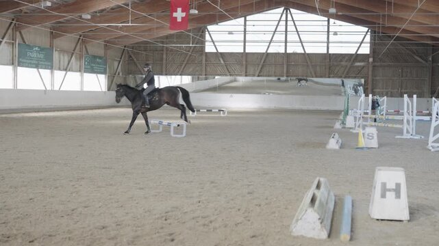 Professional jockey riding a horse during a training session inside a large indoor sandy arena