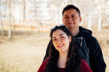 Naklejka premium Young Caucasian couple standing together outdoors with woman in front and man behind in park setting. Relationship and lifestyle theme