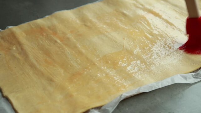 Close-up of pastry brush applying egg wash glaze to raw puff pastry dough