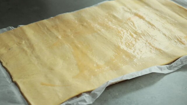 Close-up of pastry brush applying egg wash glaze to raw puff pastry dough