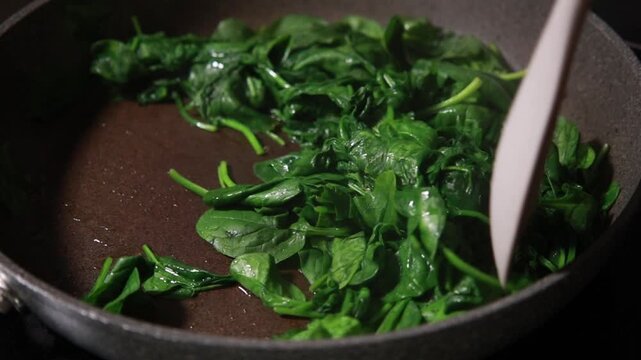 Close-up of fresh baby spinach leaves wilting and saut&eacute;ing in a hot skillet pan