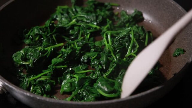 Close-up of fresh baby spinach leaves wilting and saut&eacute;ing in a hot skillet pan
