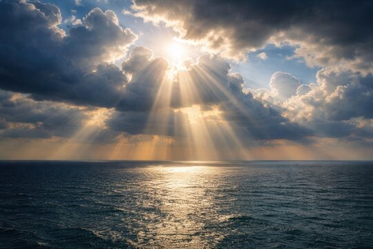Sun rays breaking through dramatic clouds over calm ocean horizon creating golden light reflection