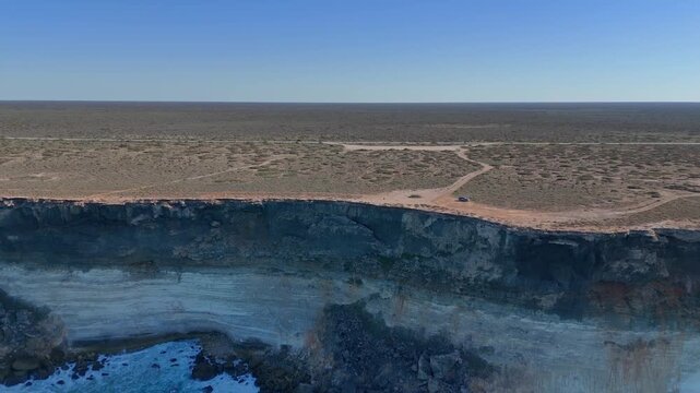 Aerial drone view pulling back from a vertical coastal cliff with waves crashing below in Australia