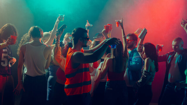 Group of people dancing and celebrating in a brightly lit club with red and blue lights. Concept of nightlife party, youth, summer, festivity, celebration