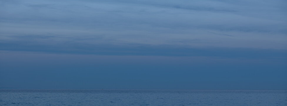 Peaceful coastal scene with gentle waves washing onto the shore and cliffs rising in the distance under a soft dusk sky. Muted tones and smooth light create a tranquil atmosphere