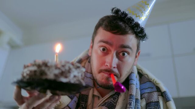 Close Up One Surprised Man In Blanket Blowing Horn Holding Cake