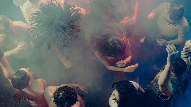 Aerial view of people dancing energetically in a smoky, vibrant club atmosphere. Concept of nightlife party, youth, summer, festivity, celebration