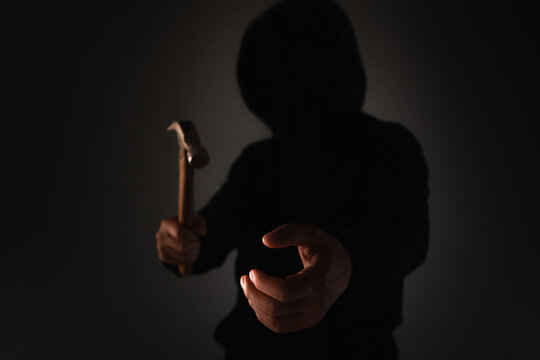 Hooded man holding a hammer in his hand on a dark background