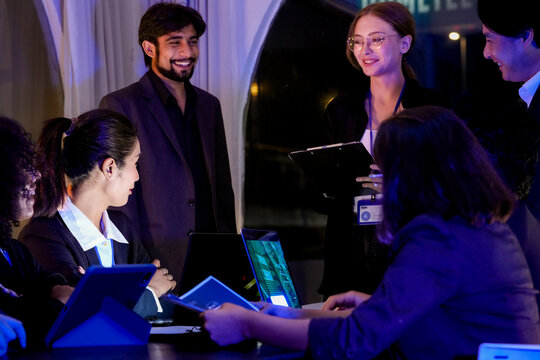 Cheerful multiethnic business professionals discussing digital strategy and celebrating milestones at night. Diverse experts sharing insights and managing software development in a creative hub.