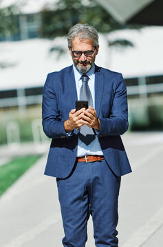 Portrait of a happy smart inteligent senior businessman smiling using a phone smartphone standing in the front of the office building