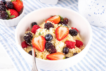Trendy Viral New Breakfast recipe Mixed Berry Couscous, alternative for traditional morning oatmeal porridge, sweet couscous with fruit and berry salad, on kitchen table, copy space © ricka_kinamoto
