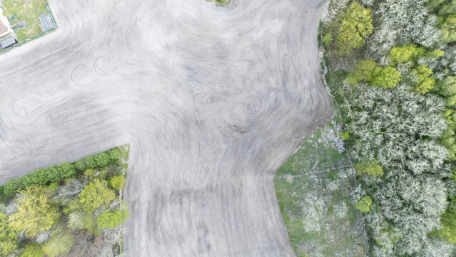 Aerial view of a tilled agricultural field with circular tire tracks bordered by lush green trees and spring vegetation Ourense, Province of Ourense, Spain.