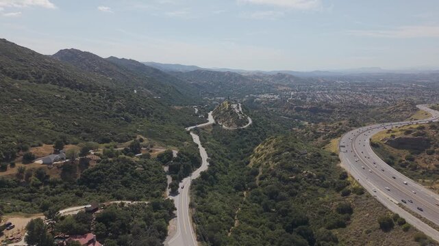 Sunny aerial view of Simi Valley, California, with cars moving along major highways between rugged hills and suburban neighborhoods under clear skies and scenic mountain surroundings.