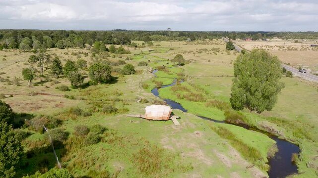 Low-altitude drone flight moving forward towards a prehistoric hut replica and stream at Monte Verde archaeological site in Puerto Montt, Chile.