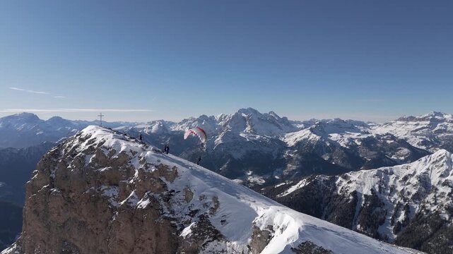Adventurers hike and paraglide on the snowy slopes of Monte Cernera, surrounded by vast mountain vistas. Ideal for adventure sports content.