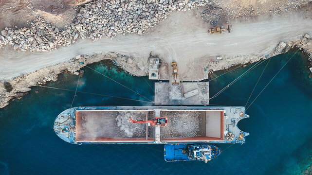 Aerial view of a large cargo ship being loaded with white stone at the Jadrankamen quarry with excavators and turquoise water in Pucisca, Splitsko-dalmatinska, Croatia.