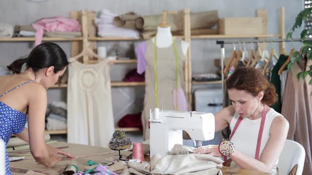 Woman tailor draw dress pattern with curve ruler on paper, female master seamstress sewing cloth with sewing machine. Tailor workplace with cut textile, sewing machine, thread, pins, needles, tape