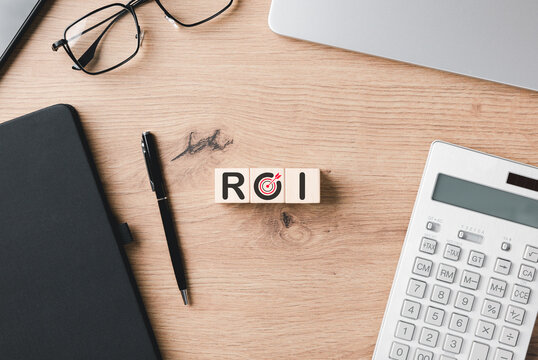 ROI return on investment concept featuring wooden blocks on an office desk with calculator and notebook to represent financial growth, profit analysis, and successful business goal marketing.