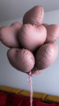Bunch of pink foil heart shaped balloons floating and gently spinning inside a room. Romantic decoration for valentine's day or a birthday party